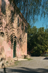 Fototapeta premium Historic pink mediterranean country house surrounded by lush vegetation and trees under a blue sky.