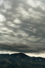 Mountains with forest on slope under a dark cloudy sky.