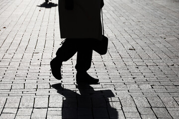 Silhouette of old woman with handbag walking down the street, black shadow on pavement. Concept of retirement life, dramatic story