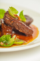 Delicious veal cheeks in red sauce with green. Closeup on a white plate on white background