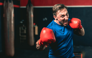 A boxer is doing shadow boxing. He is wearing blue shirt and red boxing glove. He is working really hard punching the air.
