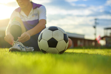 Sport man tying shoes with classic ball before playing soccer football on green grass field. Athlete sportman player and exercise concept.