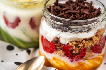 Closeup 2 glass with yogurt, fruit (raspberry, pistachio, mango), granola and grated chocolate.