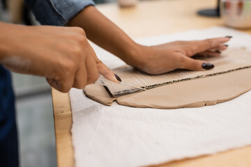 cropped view of african american woman cutting clay with knife near carton.