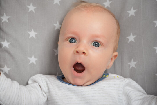 Portrait of surprised newborn baby with open mouth, close-up. Cut child with blue eyes, looking at camera. Face expression.