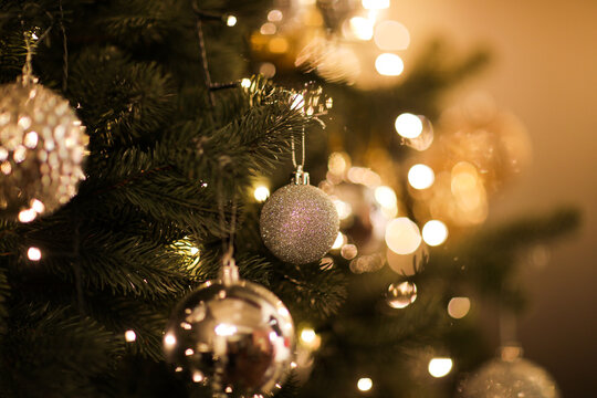 Close up view of beautiful fir branches with shiny golden bauble or ball, xmas ornaments and lights, Christmas holidays background. copy space. Decoration on christmas tree. Festive new 2023 year
