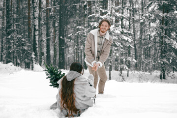Sledging love romantic young couple girl,guy in snowy winter forest with christmas tree, sled.Walking with sleigh in stylish clothes, fur coat,jacket,woolen shawl.Snow lovestory.Romantic date,weekend