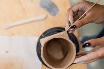 Fototapeta na wymiar Top view of african american craftswoman making ceramic product with wooden stick in pottery studio.