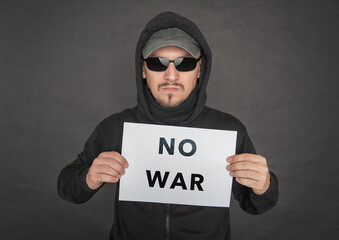 Man in the black hoody with hood wearing sunglasses holding no war on white sheet of paper