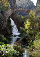 waterfall flowing under the historical bridge and river in greenery