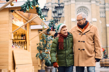 Fototapeta premium Embraced grandfather and grandson walking through Christmas market during winter holidays.