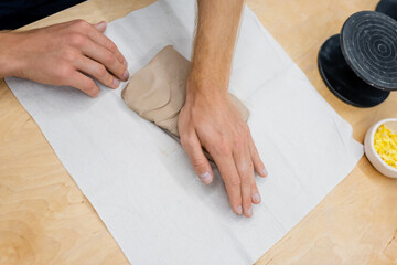 top view of cropped man pressing clay piece with hand during pottery class.