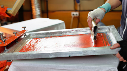 silk screen print. male hand with a squeegee. serigraphy production selective focus photo. printing images on clothes by silk screen method in a design studio