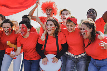 Multiethnic friends football supporter fans watching soccer match at stadium -  People with red...