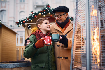 Happy grandfather and grandson toasting while drinking tea at Christmas market during winter day.