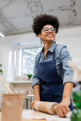 cheerful african american woman in eyeglasses and apron modeling clay with rolling pin.