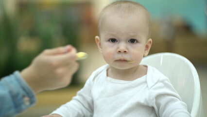 Mom feeds the baby puree from a small spoon. Mother and one year old son eating at the food court - 537849377