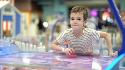 A boy of seven years old enjoys playing air hockey in the playground for entertainment - 537849577
