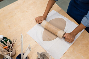 top view of african american woman modeling clay piece with rolling pin during pottery class.