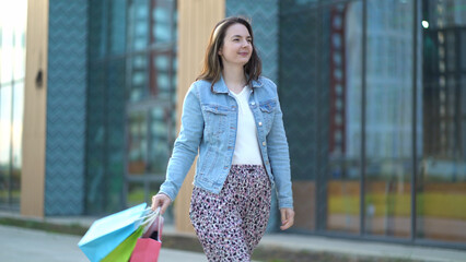 Joyful satisfied woman goes after shopping. A young girl holds bags of different colors in her hands - 537849978
