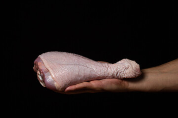A man's hand holds a raw turkey leg on a black background. Fresh turkey meat