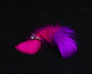 Silver engagement ring with diamond on pink feather. White gold ring with gemstone on black background