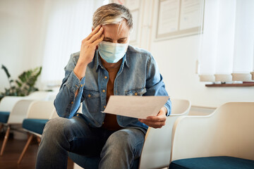Worried man with face mask reads his medical report in waiting room at doctor's office.