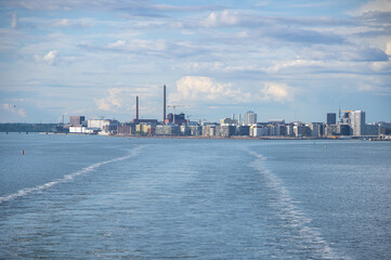 Fototapeta premium View from the sea to Helsinki skyline on summer evening. Water trail behind ferry in the Baltic sea in the foreground