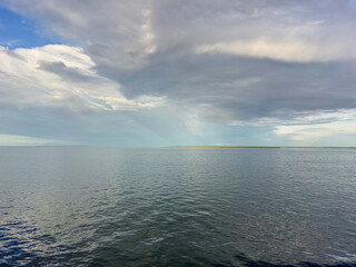 Beautiful clouds over the Baltic sea in summer evening. Estonian coast on the horizon lit by evening sun