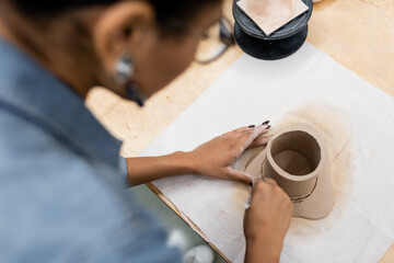 top view of african american woman shaping clay cup during pottery class.