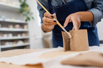 cropped view of african american woman in apron holding shaper while modeling clay.