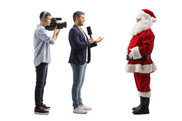 Full length profile shot of a male journalist and a cameraman interviewing santa claus - obrazy, fototapety, plakaty
