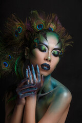 Beautiful Asian girl with creative makeup in the form of a peacock on a dark background.