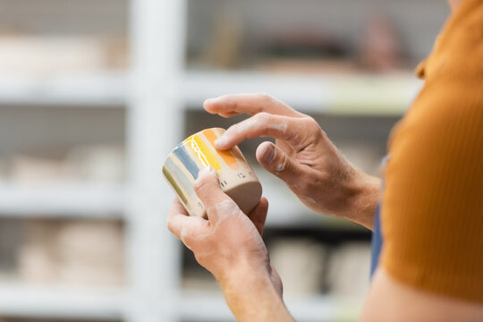 Cropped view of craftsman holding ceramic cup in pottery workshop.