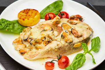 Delicious baked salmon steak with cream sauce and mussels is served on a plate and ready to eat. Restaurant menu position