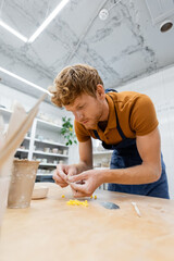 Young artisan in apron holding pottery tools in workshop.