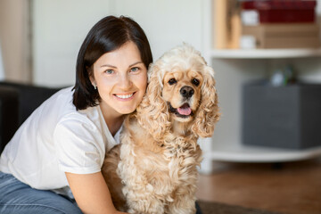 Attractive young brunette hugs her American cocker spaniel dog sitting at home on the floor. the concept of love for pets