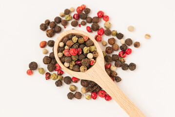 Macro photo of a mixture peppers  in wooden spoon scattered on a white background isolated, top view