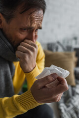 sick man in warm scarf holding paper napkin and sneezing at home.