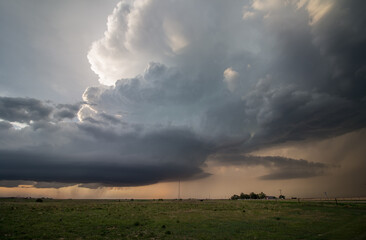 A towering supercell thunderstorm, or cumulonimbus cloud, moves over the prairie near sunset.