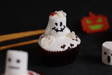 delicious chocolate cupcakes with white cream and marshmallows painted with funny faces on a dark...