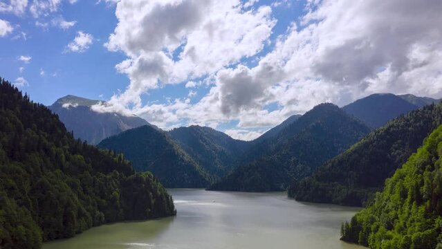 Aerial view of floating clouds over lake and mountains. Drone Time-lapse Footage of white clouds moving over water. Flight under the clouds. Aerial view