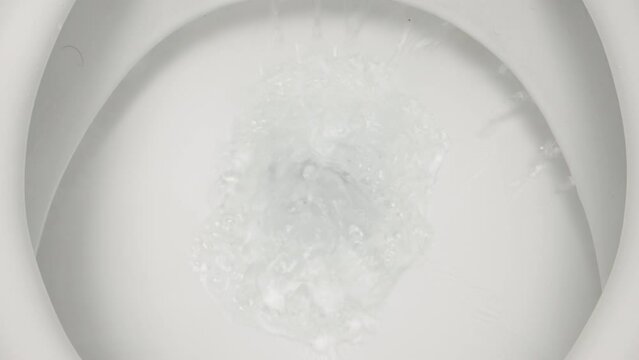 The camera looks into the toilet while the water is being flushed there. Close-up