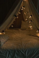 Camping tent bed decorated with Christmas lights. Kid's bedroom. Winter holidays. Evening...