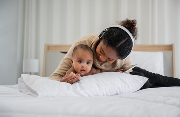 Happy African newborn baby lying on tummy on pillow with smile and looking at camera on bed at home.