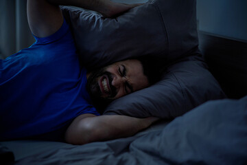 A young arab man holds a pillow with two hands covering his ears from the loud noise at home, a sleepless night, close-up with free space