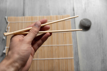 wooden chopsticks for rolls and sushi in a man's hand against the background of a roll mat