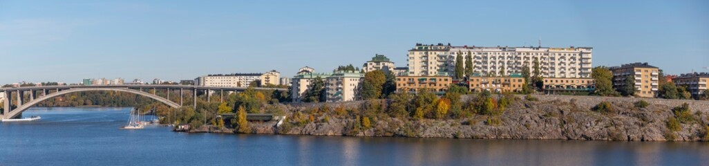 Fototapeta na wymiar Panorama view at a bay of the lake Mälaren, water front apartment houses on a cliff and a long high bridge a sunny a color full autumn day in Stockholm