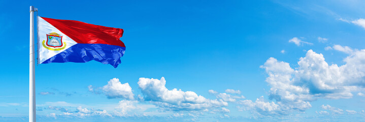 Sint Maarten flag waving on a blue sky in beautiful clouds - Horizontal banner