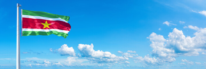 Suriname flag waving on a blue sky in beautiful clouds - Horizontal banner